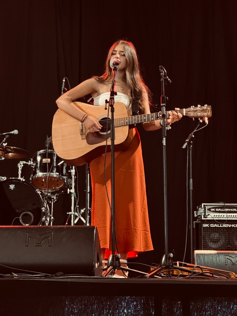 Ava Turnbull performing live on stage with acoustic guitar